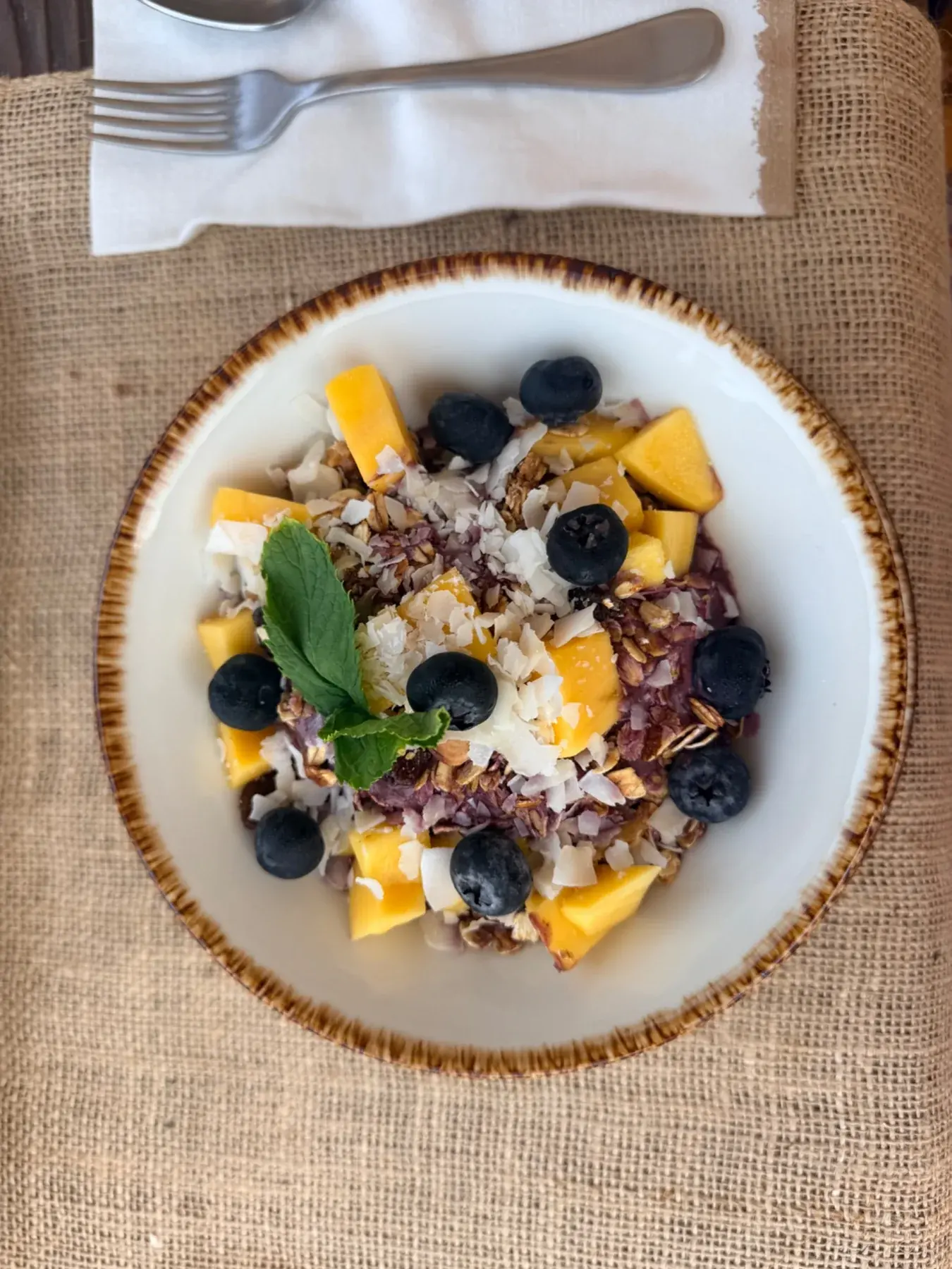 Ontbijtbowl met yoghurt, mango en blauwe bessen op een jute placemat